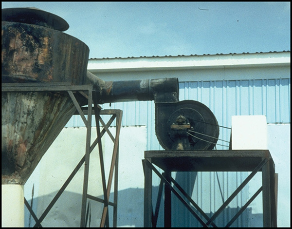 A fan and collector purchased at a salvage auction. The owner used a 50-gal. drum as part of the duct system between the fan and collector. In addition to a base that is unstable, there is no length of ductwork at the fan outlet to establish uniform airflow.